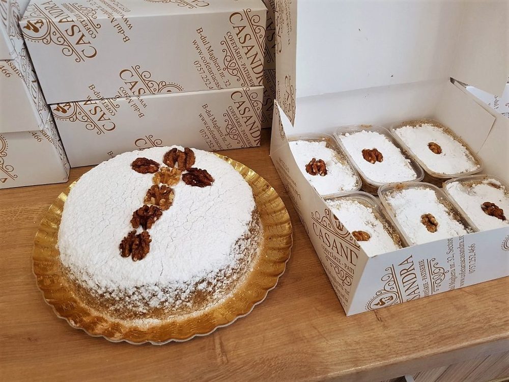 Cutii albe cu sigla aurie Casandra și un tort cu nucă, în cofetărie